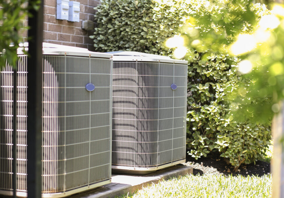 Air conditioner unit outdoors in side yard of a brick home in hot summer season.   No people.